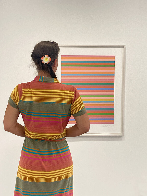 Eine Frau betrachtet ein Kunstwerk der Künstlerin Bridget Riley