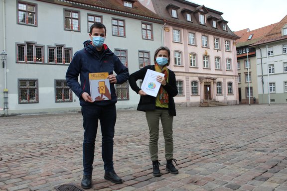 Simon Höge und Annette Hug-Kalisch von der Stadt stehen vor dem Rathaus und zeigen den Integrationsbericht und die Broschüre für Flüchtlinge.