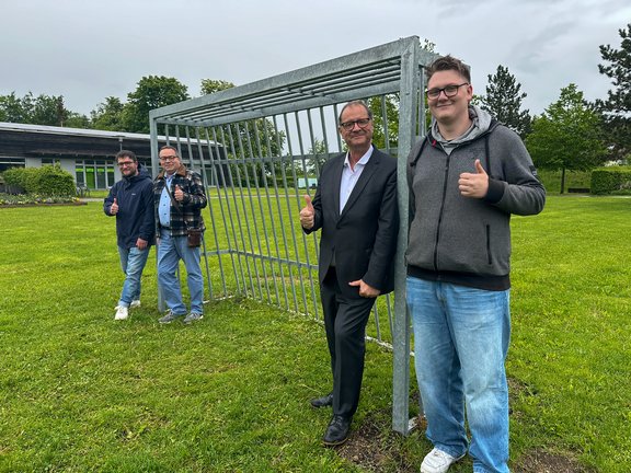 Oberbürgermeister Jürgen Roth (Zweiter von rechts), Jonas Hilsenbeck (JuBiS, von links), Armin Scherzinger (GuT) und Tim Dippong vom Jugendgemeinderat stehen vor einem Metalltor, das neu aufgestellt wurde.