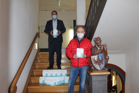 Alexander Lees vom Sport Bubi und Oberbürgermeister Jürgen Roth stehen auf einer Treppe im Rathaus Villingen, zwischen ihnen liegen FFP2 Masken für Kinder.